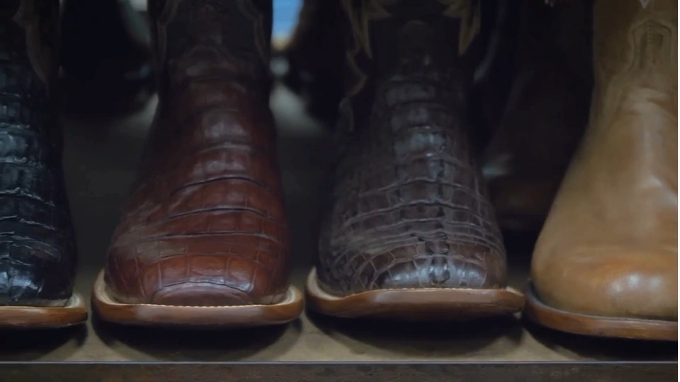 A row of square-toe caiman and leather western boots lined up on a store shelf.
