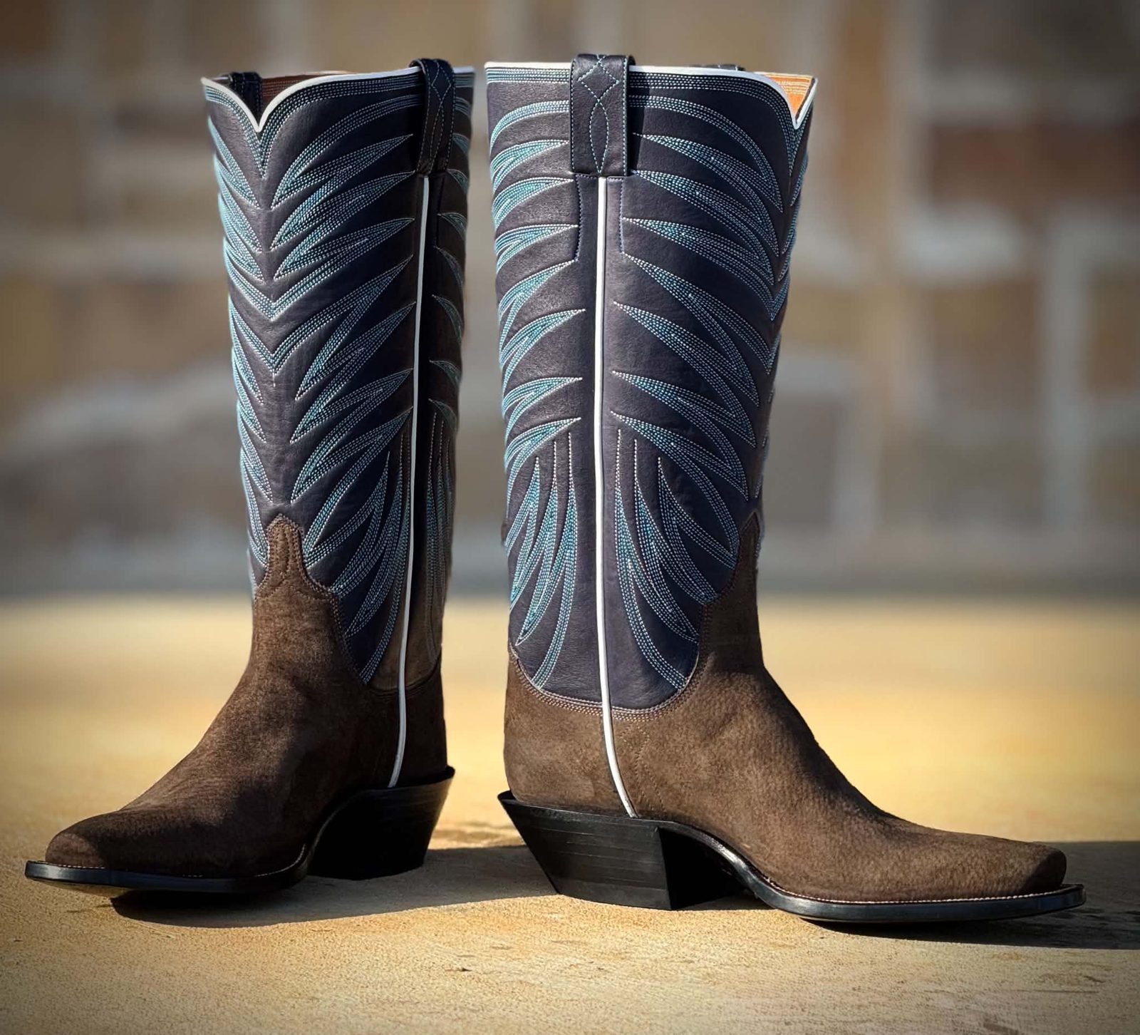 Navy boot tops with pale blue ribcage stitching over brown roughout vamps in low sunlight