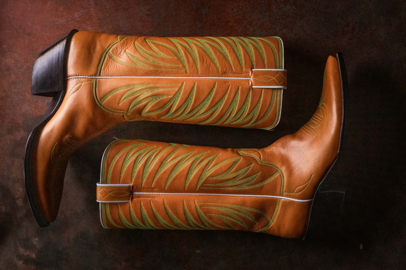 A tan pair laid on its side showing green flame stitching down the shafts and white piping